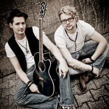 Hofi (Daniel Maierhofer) mit Gitarre und Manu (Manuel Riedl) sitzen